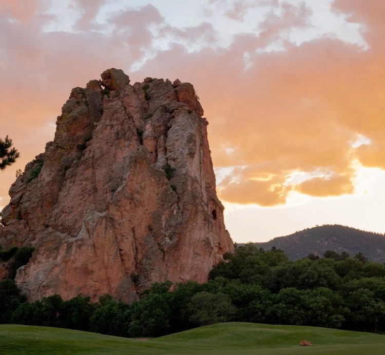 Large rocky formation against a sunset sky with green landscape.